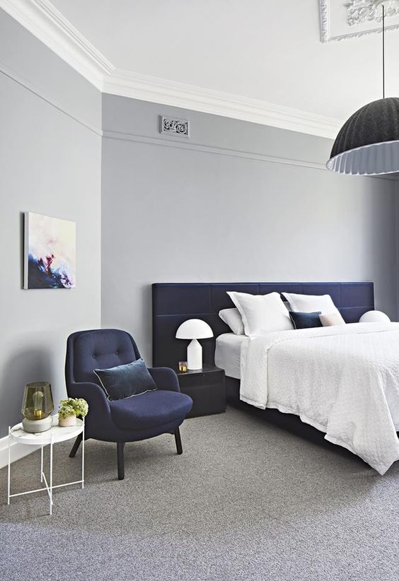 an airy bedroom in light grey with a navy upholstered bed and chair for a bold look
