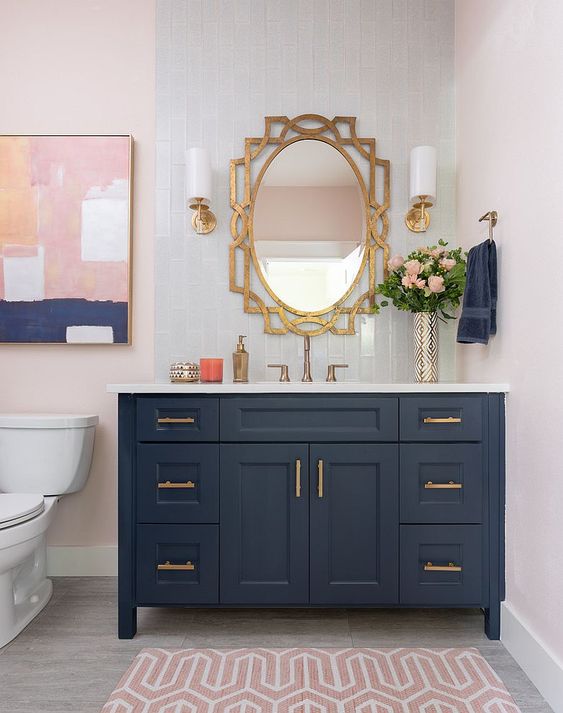 a stylish bathroom with a navy vanity, a blush printed rug and a catchy artwork that ties them both