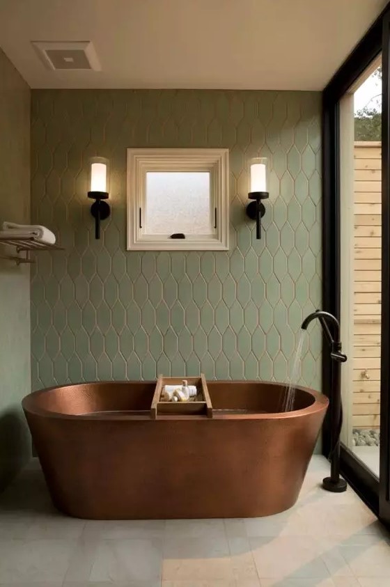 a beautiful modern spa bathroom clad with neutral and green tiles, with a glazed wall, an oval copper tub and black fixtures