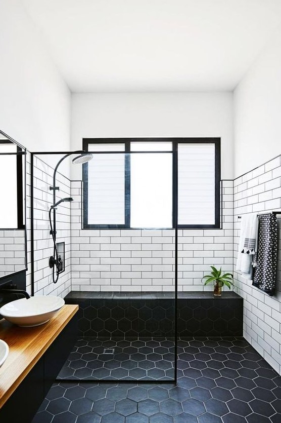 a bold monochromatic bathroom with white subway tiles and black hex ones, a floating vanity and bowl sinks plus black fixtures