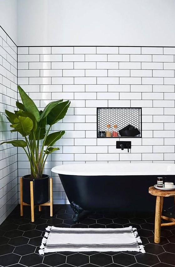 a contrasting bathroom with white subway tiles and black hex ones, a black clawfoot tub and wooden furniture