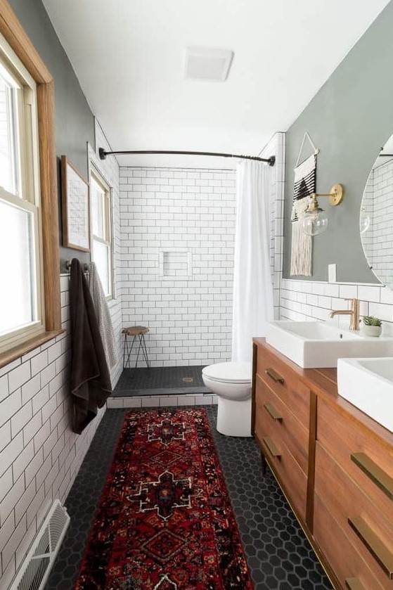 a cozy mid-century modern bathroom with white subway and black hex tiles, with a wooden vanity, a boho rug and windows