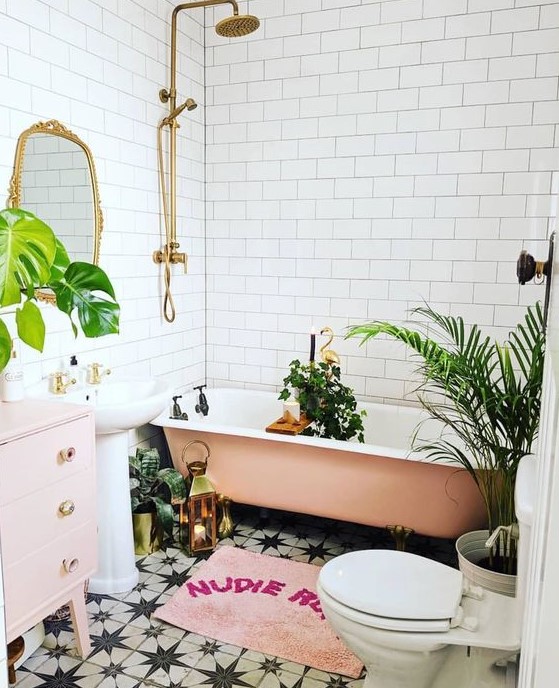 a glam tropical bathroom in neutrals, a pink tub, a pale pink vanity, a pink rug and potted plants, gold touches