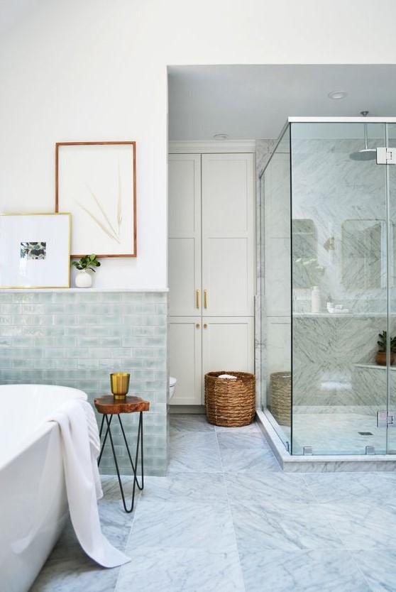 a lovely coastal bathroom with aqua glazed tiles, a shower clad with grey marble tiles, touches of wood and a basket