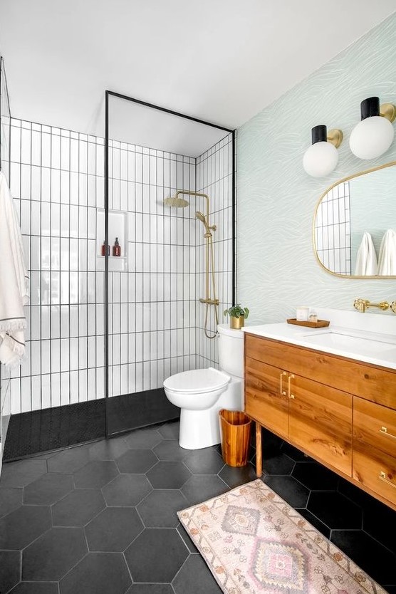 a mid-century modern bathroom with white skinny and black hex tiles, a stained vanity, a blue accent wall, gold fixtures