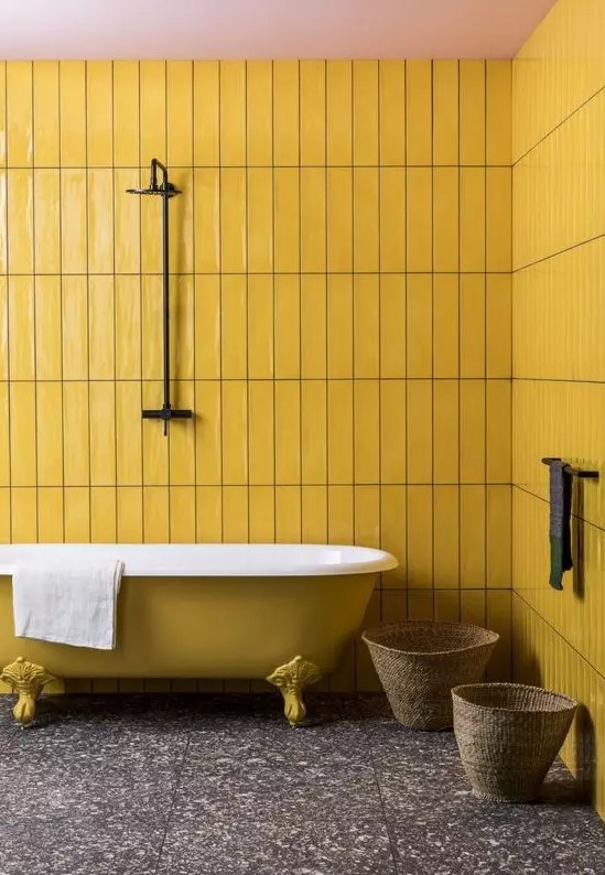 a minimal bathroom with mustard tile walls and a mustard bathtub, a dark stone tile floor and baskets