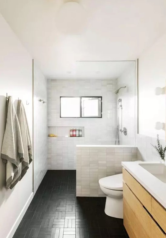 a modern bathroom with marble skinny tiles and black ones on the floor, a floating wooden vanity, a built-in niche for storage