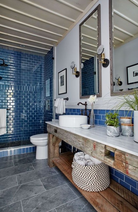 a modern beach bathroom with a shower clad with bright blue tiles, a round sink, vintage faucets and a gorgeous weathered wood vanity