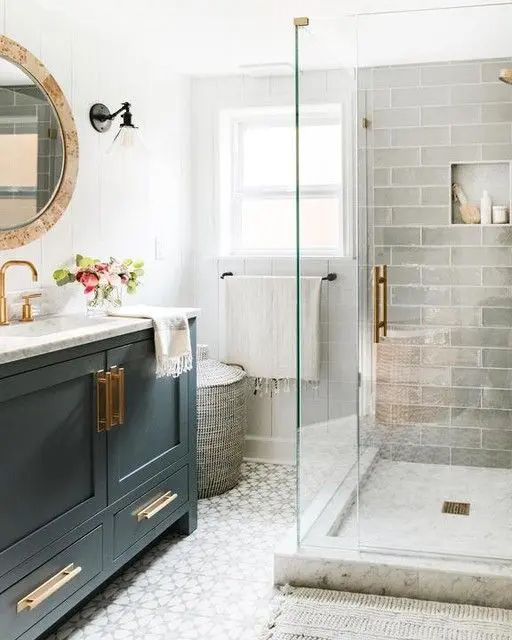 a modern farmhouse bathroom with printed and grey subway tiles, a black vanity, a round mirror, a shower space and a basket