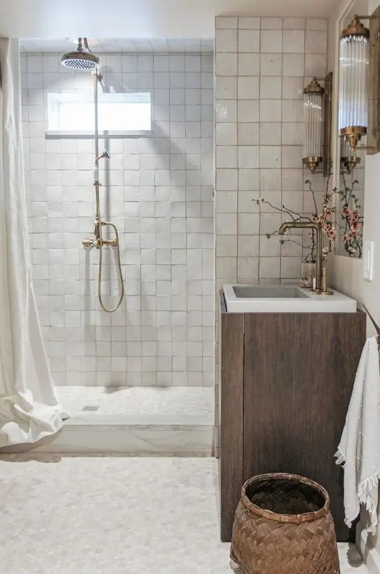 a neutral bathroom clad with neutral zellige tiles, a timber vanity, a mirror, some lovely vintage sonces and a basket