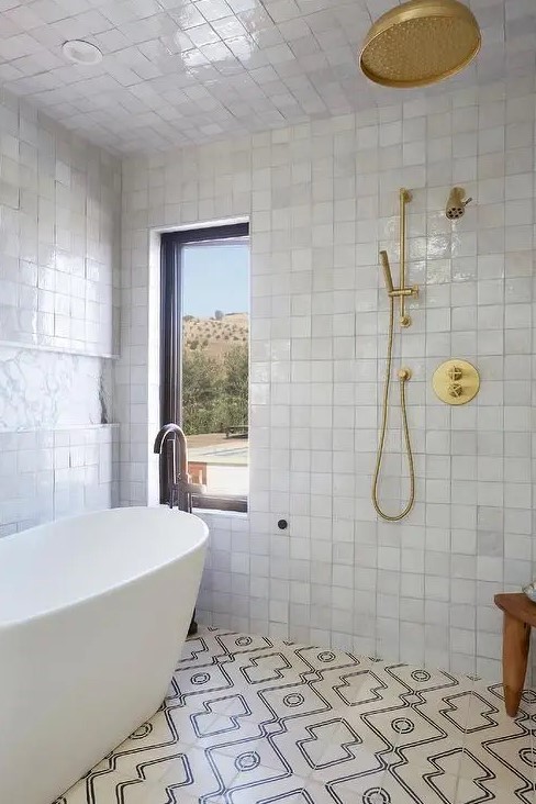 a neutral bathroom with white Zellige tiles and geometric ones, an oval tub and brass and gold fixtures