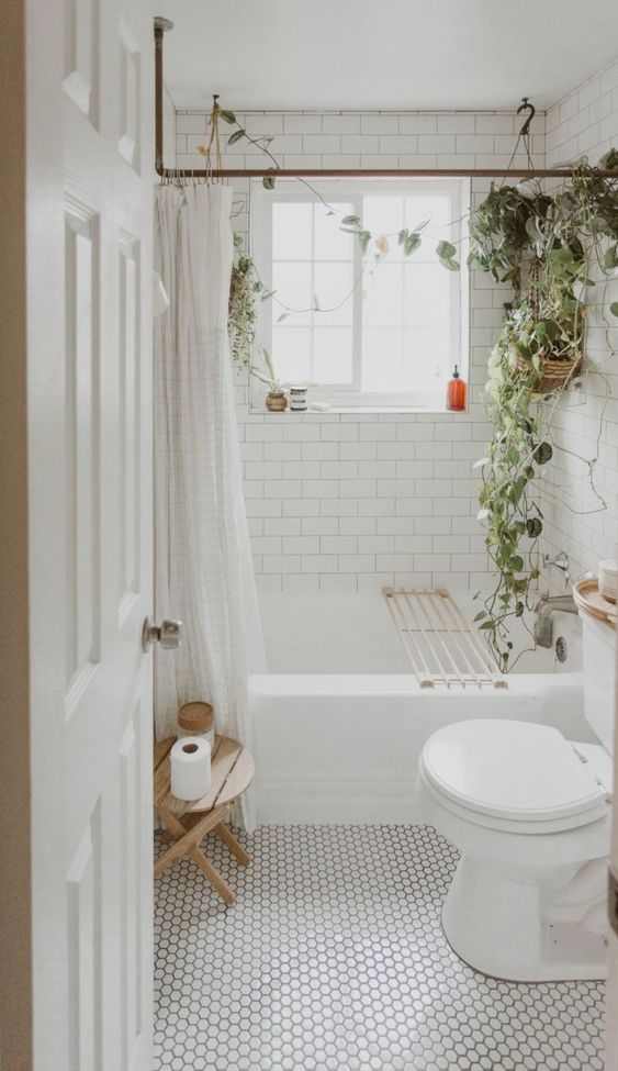 a neutral boho bathroom with white penny and subway tiles, a bathtub, potted greenery, a stained stool is welcoming