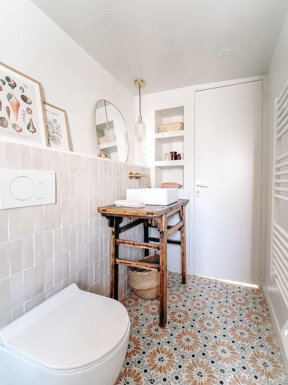 a powder room with peachy and rust and mint tiles, a wooden vanity, niche shelves and some artwork