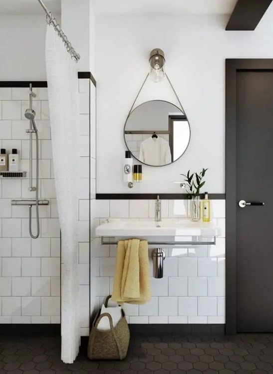 a stylish white and graphite grey mid-century modern bathroom with grey hex tiles on the floor and a round mirror and a floating sink