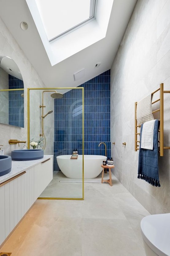 an ocean-inspired bathroom with a skylight, large format tiles, a navy accent wall, a floating vanity with navy sinks and gold touches