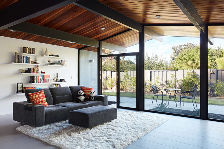 The living room is done with a grey sofa, an ottoman, some open shelving and a fluffy rug