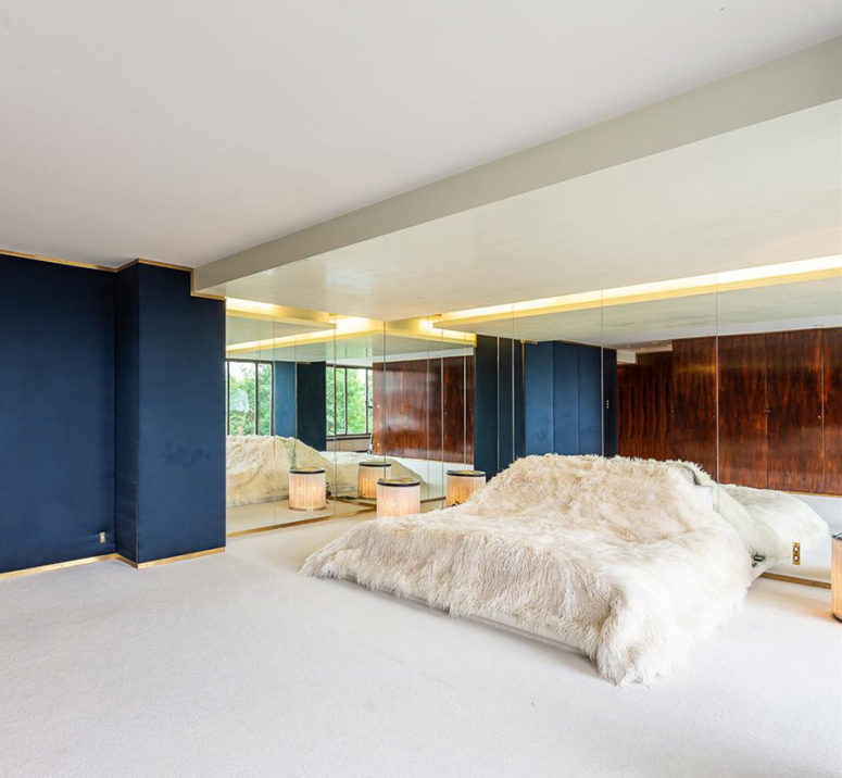 The master bedroom is done with a large bed, mirror walls and much negative space for an airy feeling