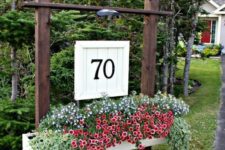 09 a large outdoor planter on stands with lush blooms and greenery and a wooden plaque with house numbers and an additional light