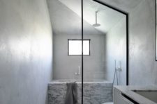 10 There’s a large marble clad bathtub and cocnrete walls plus a window that brings light in