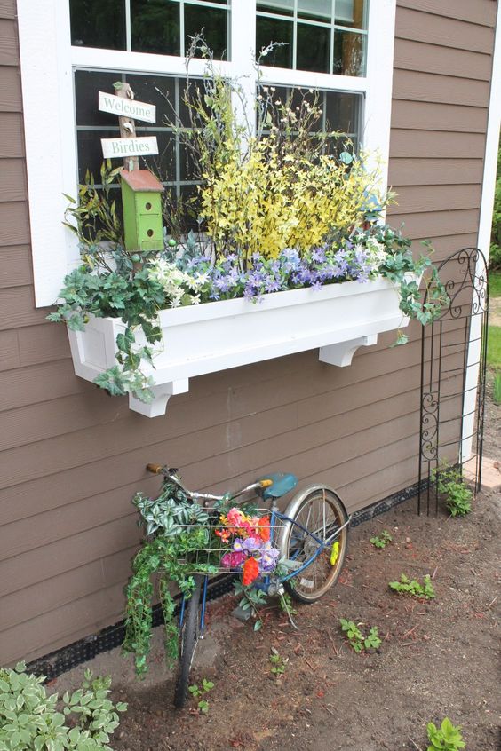 a white window box planter with pastel spring blooms and a little bird house for more coziness and sweetness