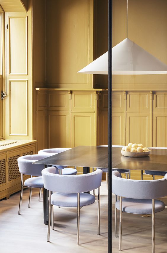 a dining space with yellow walls and lilac and brass chairs with a laconic and modern design