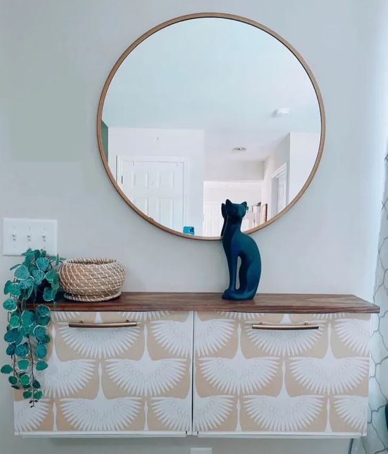 a modern boho entryway with a Trones piece covered with wallpaper, greenery, a woven planter, a black cat and a round mirror
