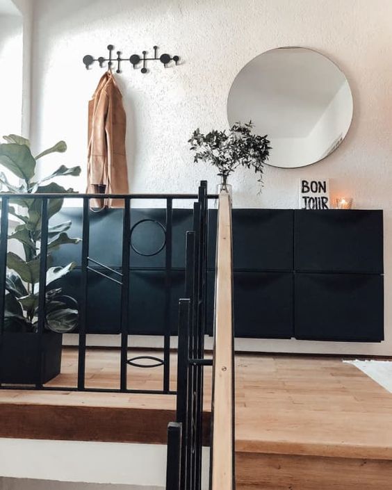 a modern entryway with a black Trones cabinet, a round mirror, a rack and a potted plant and a candle