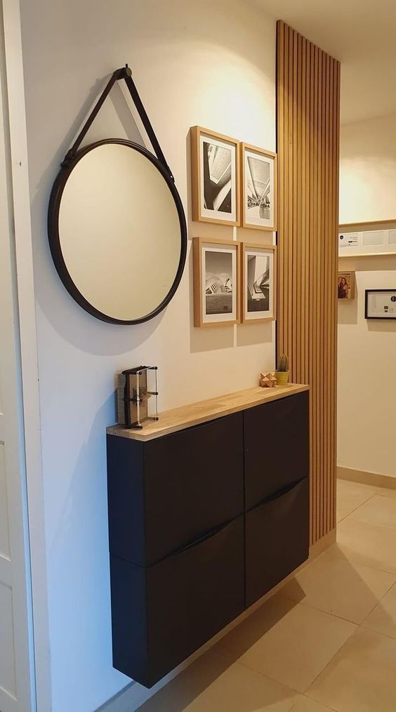 a modern entryway with a black Trones piece with a wooden countertop, some decor and a round mirror, a black and white gallery wall
