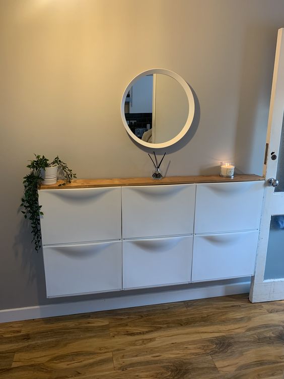 a modern hallway with a white IKEA Trones piece with a wooden countertop, candles, a potted plant and a small mirror