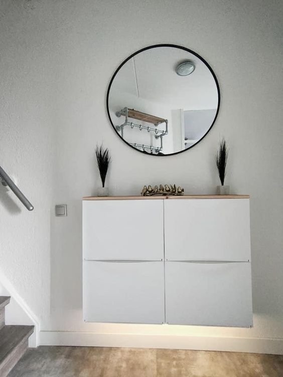 a small nook with a white Trones piece with built-in lights and a wooden countertop, a round mirror, grasses and gold birds