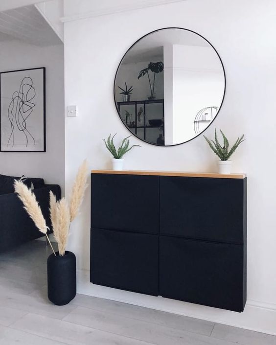 a stylish boho space with a black Trones cabinet with a wooden countertop, a round mirror, a black vase with pampas grass and potted plants