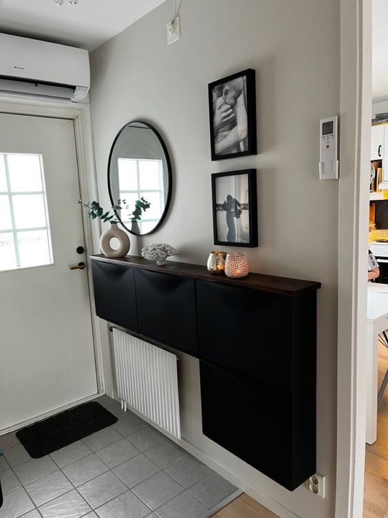 a stylish modern entryway with a black Trones and a radiator, black and white photos, a round mirror and some candles