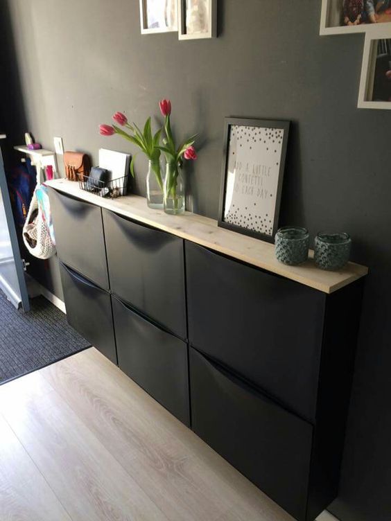 a stylish modern entryway with a black wall, a black Trones piece, blooms, decor and artwork is a catchy space