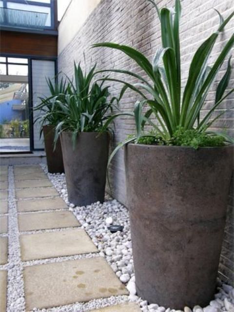 oversized concrete planters with the same plants placed on contrastign white pebbles is a bold idea