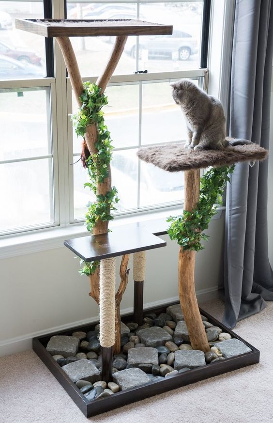 a modern cat tree of tree branches decorated with fake greenery, of several platforms and a base with rocks and pebbles