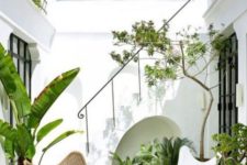 11 a small tropical patio with lots of potted plants, a white and wicker butterfly chair and all white walls around