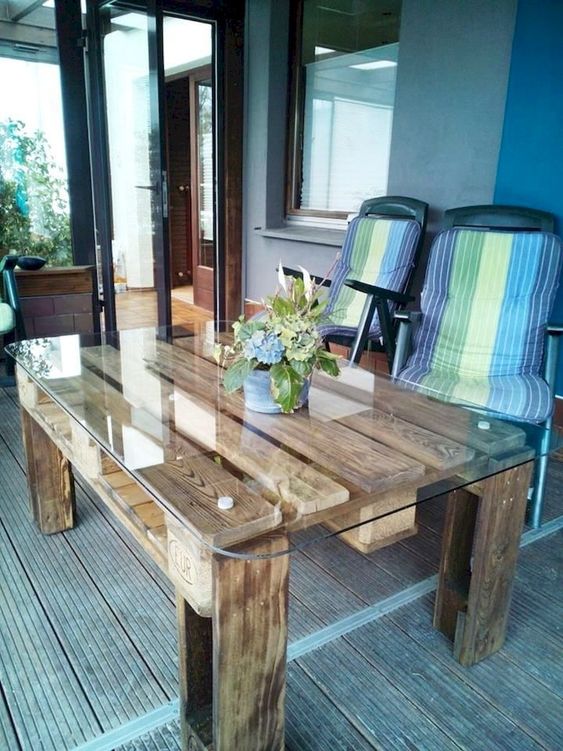 an outdoor contemporary meets rustic dining table of stained pallet wood and with a glass tabletop
