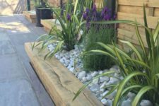 13 a wooden garden bed edge, bright flowers and greenery all covered with neutral pebbles on top