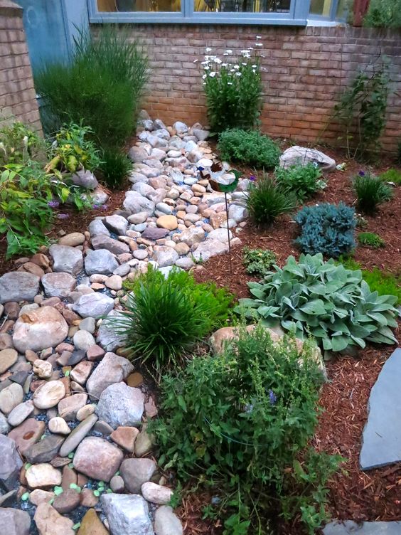 a dry stream idea with large pebbles and rocks plus green grasses around and some blooms