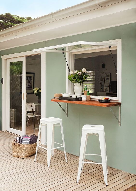 a garage-style window, a small tabletop, white metal stools for a comfy and cozy outdoor bar