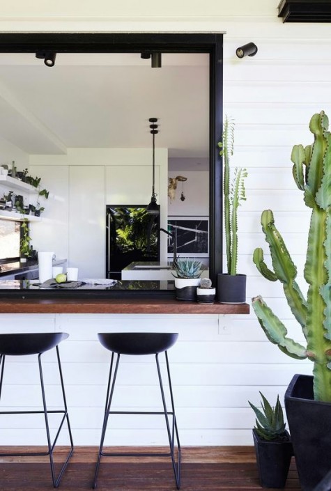 a sliding black framed window and a dark stained tabletop with cacti, black metal stools for a chic look