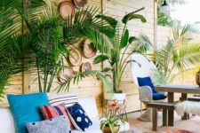 22 a tropical boho patio with potted plants, a white sofa, boho rugs and an ottoman, a living edge table and decorative baskets on the wall