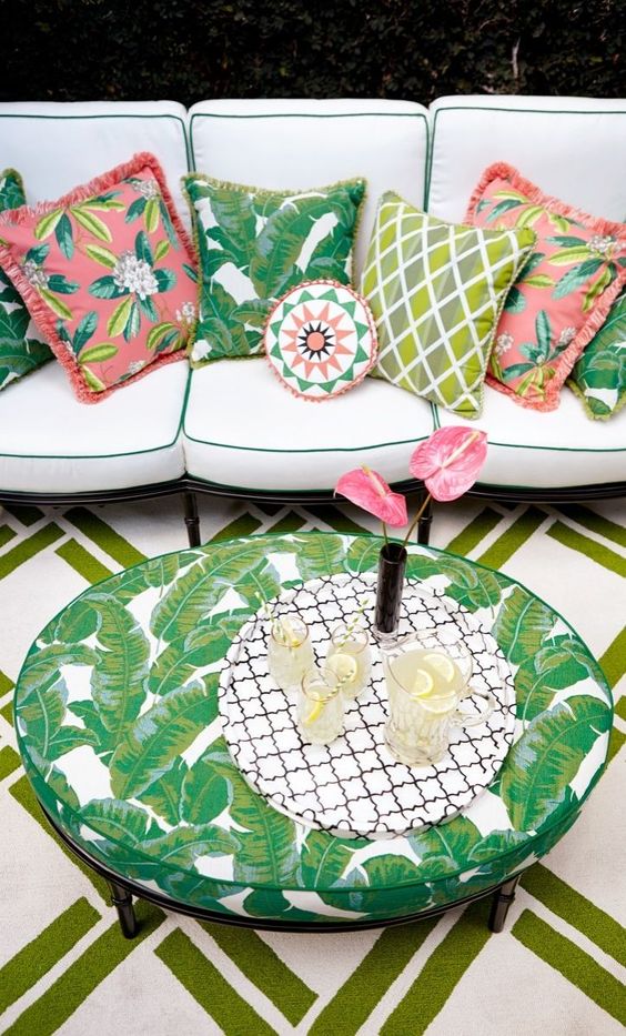 trang trí lá nhiệt đới tạo nên một sân hiên boho với một chiếc ghế sofa lớn màu trung tính với gối đầy màu sắc và một bàn in hình lá nhiệt đới