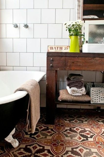 a boho meets rustic bathroom with mosaic tiles on the floor, a wooden vanity and a large black tub