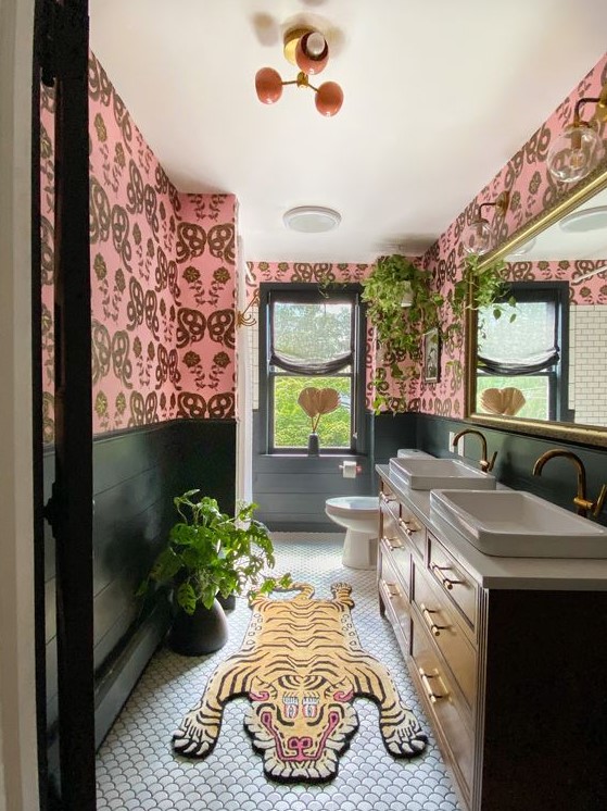 a bold eclectic bathroom with pink wallpaper walls, a stained vanity with two sinks, a bold and colorful rug and potted plants