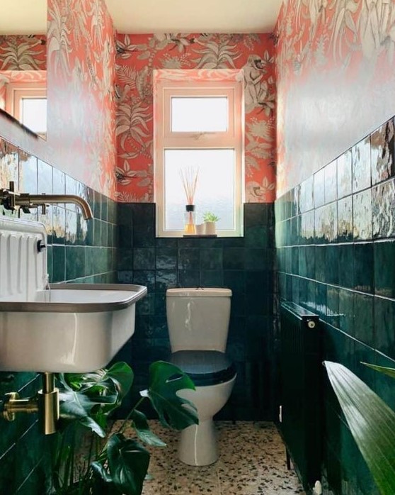 a bold maximalist bathroom with red floral wallpaper, dark green tiles, statement plants brass touches