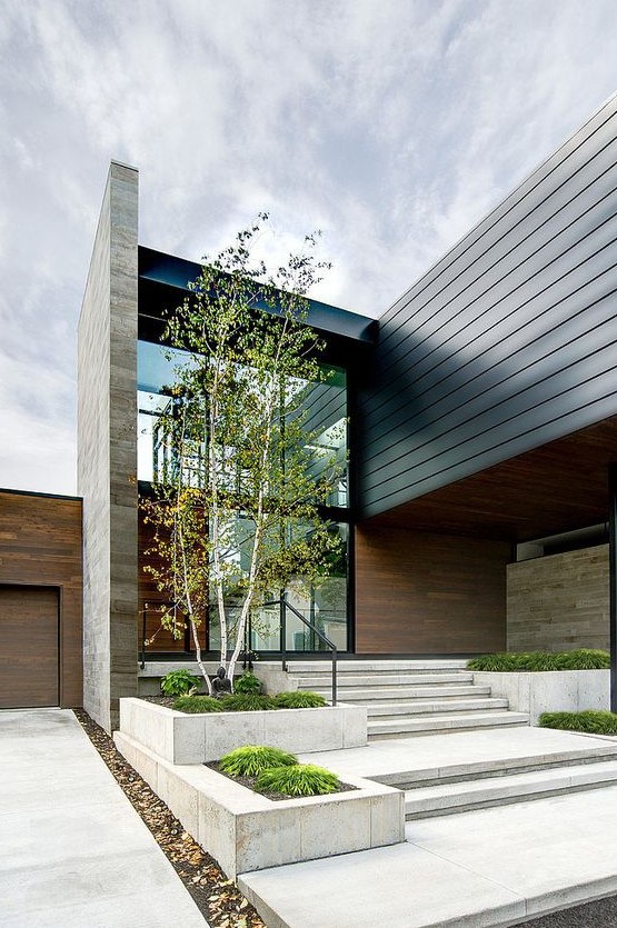 a bold modern front yard all clad with stone tiles, with greenery in stone flower boxes, with a tree and a sculpture is a statement space