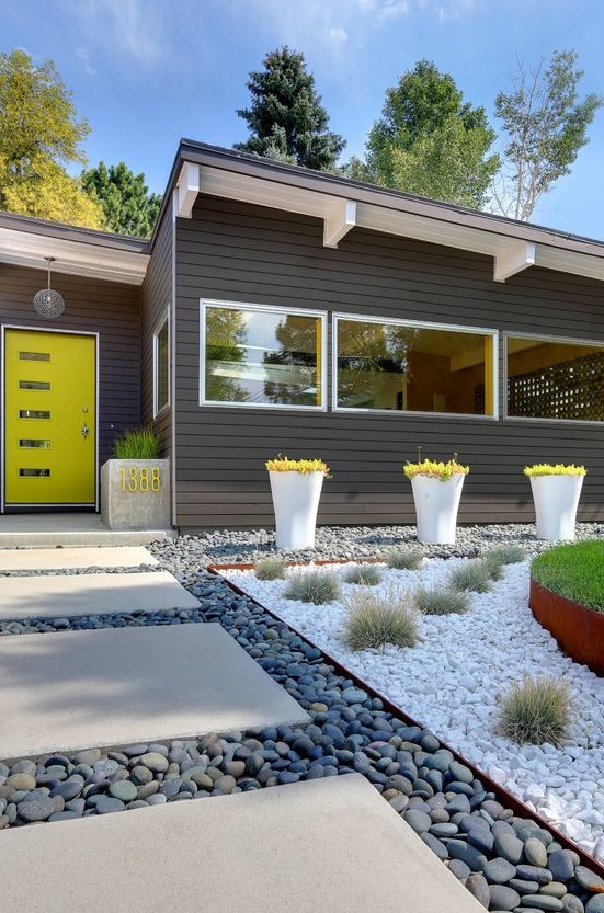 a bright and cool modern front yard with pebbles, tiles, grass balls and bold greenery in tall planters plus a planter with a neon house number