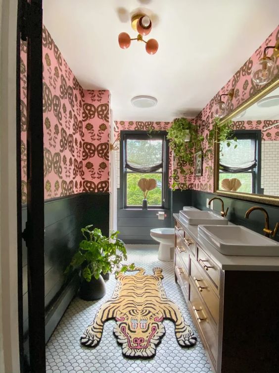 a bright eclectic bathroom with black wall paneling, pink wallpaper, a black vanity, a large mirror and potted greenery