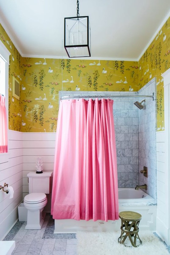 a bright eclectic bathroom with mustard wallpaper and bird print, a bathing space with a pink curtain and a pink curtain on the window, white planks and white marble tiles